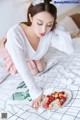 A woman sitting on a bed with a plate of cherries.