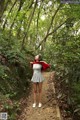 A woman standing in the middle of a forest holding a red scarf.