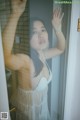 A woman in a white lingerie standing in front of a glass door.