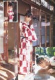 A woman in a red and white kimono leaning against a window.