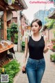 A woman in a black tank top and jeans walking down a street.