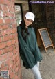 A woman leaning against a brick wall wearing a white hat.