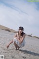 A woman in a white dress sitting on a sandy beach.